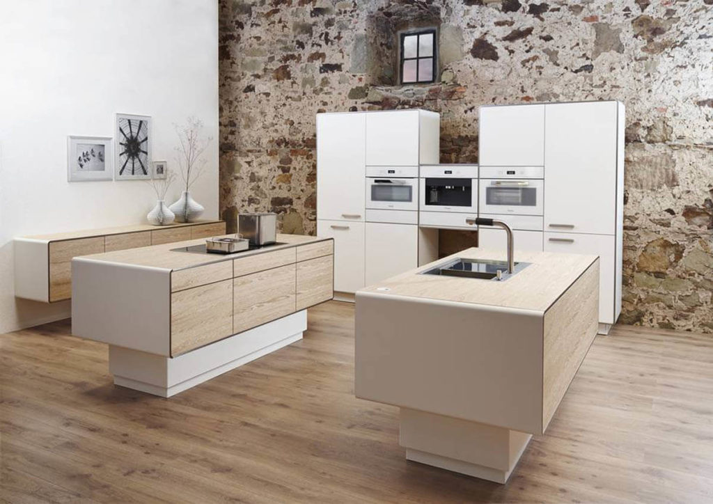 Diese Inselküche hat sogar zwei Kochinseln aus Holz (Eiche Furnier) und einer Zeile mit weißen Hochschränken (Diamantlack Weiß). Foto: Allmilmö