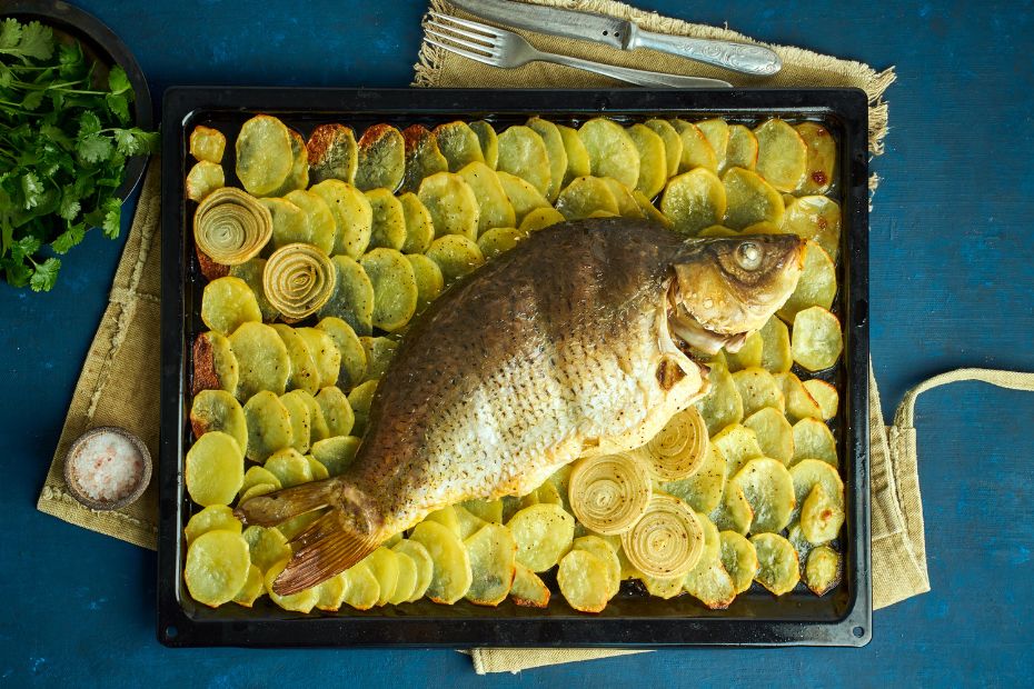Ganze Dorade aus dem Ofen mit Kartoffelscheiben, Zwiebeln und Knoblauch auf einem Backblech.