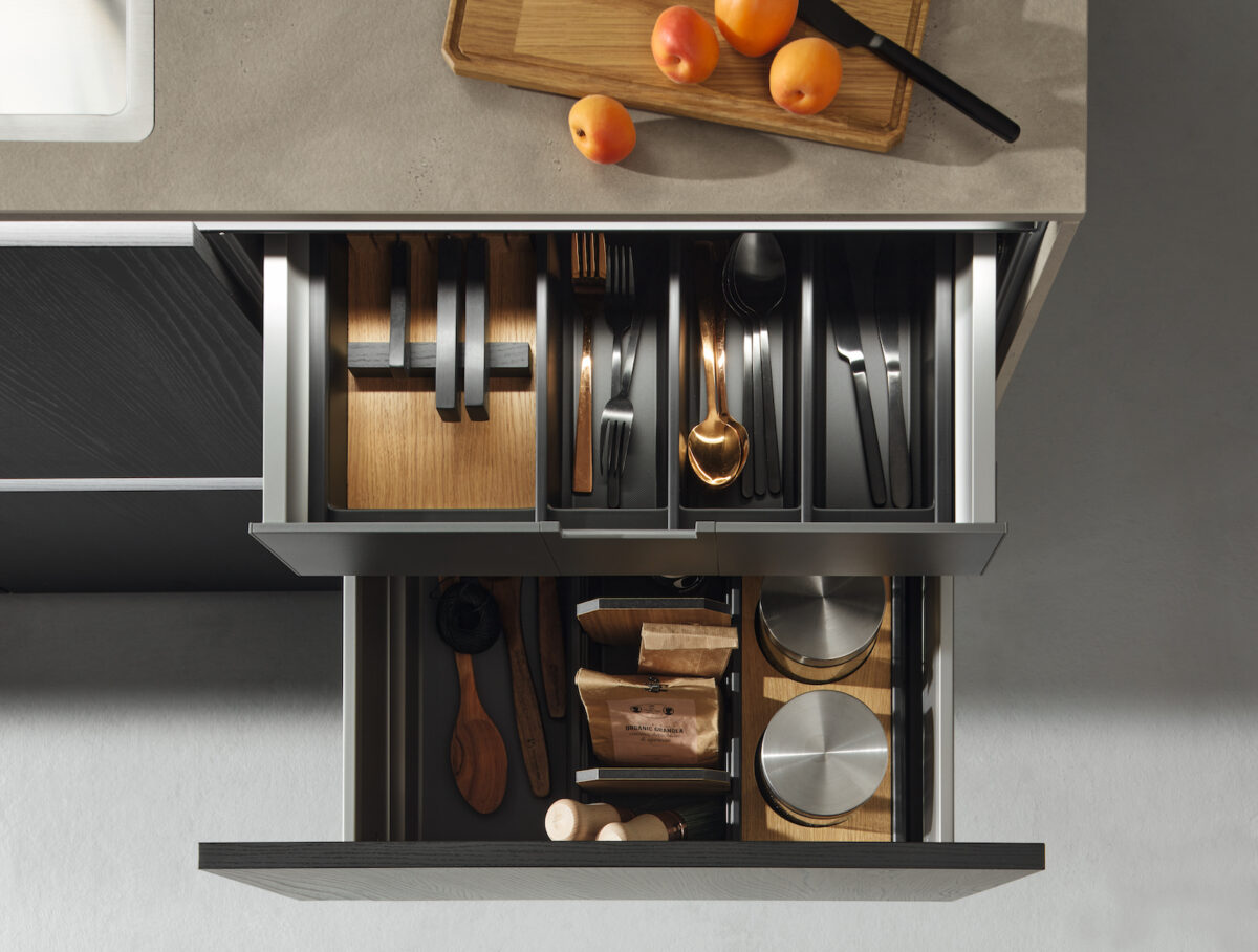Zwei offene Küchenschubladen übereinander, die mit einem Einsatz aus Echtholz in ESCHE schwarz von Nolte Küchen ausgestattet sind. 