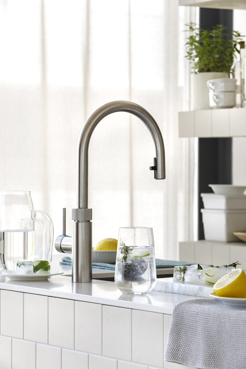 Moderne Küchenarmatur von Quooker mit CO₂-Zusatz für gekühltes Sprudelwasser. Daneben steht ein Glas mit Kräutern und Eiswürfeln.