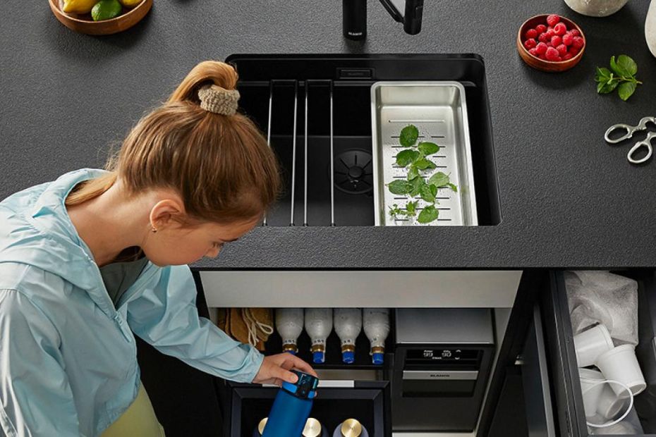 Frau nutzt BLANCO UNIT mit schwarzer Spüle, integrierten Kräutereinsatz und Wassersystem im Unterschrank mit Flaschenorganisation