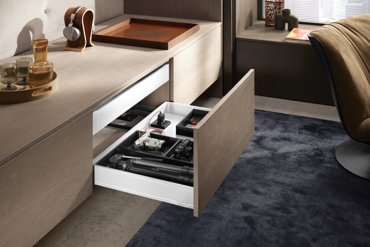 Geöffnete Schublade in einem Wohnmöbel, ausgestattet mit AMPEROS AC zur unsichtbaren Stromversorgung, in der Kameraausrüstung ordentlich verstaut und geladen wird.