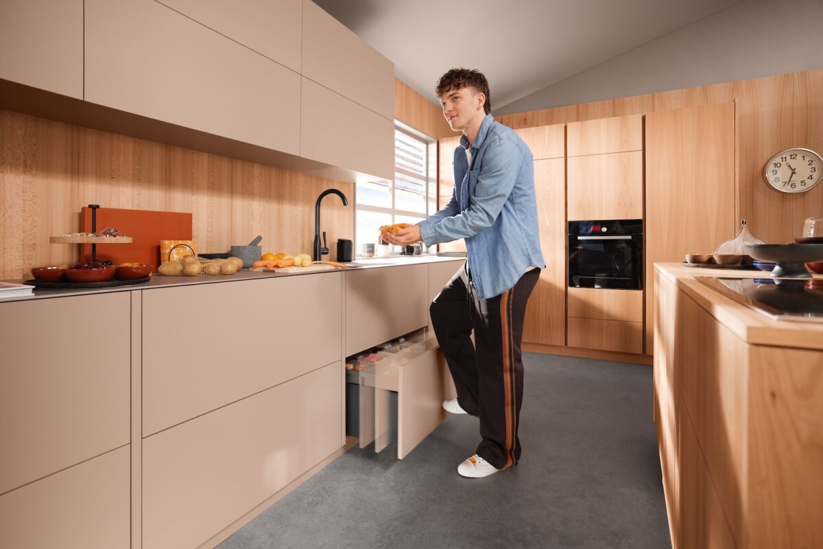 Person in einer hellen Küche, die den Müllauszug per leichtem Antippen mit dem Knie über die elektrische Öffnungsunterstützung SERVO-DRIVE uno öffnet.