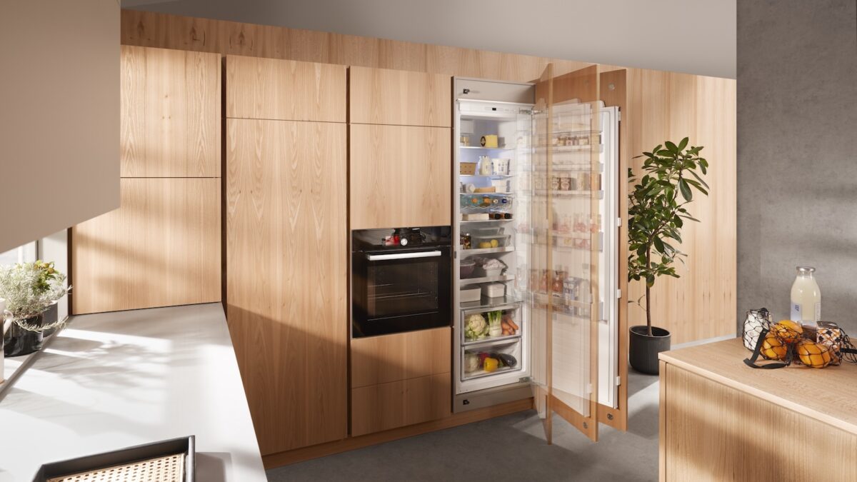 In einer modernen Holzküche öffnet sich die hohe Kühlschrankfront dank SERVO-DRIVE flex automatisch nach einem leichten Antippen.