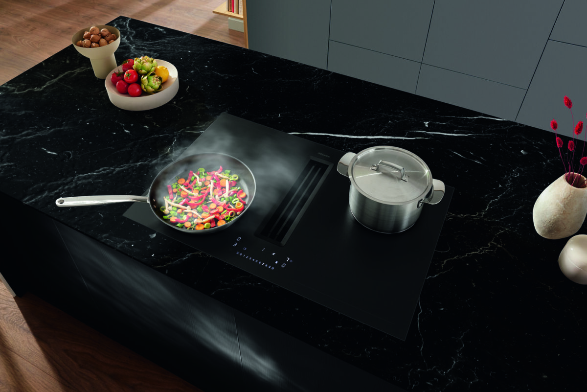 Mattes Induktionskochfeld mit integriertem Muldenlüfter und dunkler, strukturierter Glasoberfläche in moderner Küche.