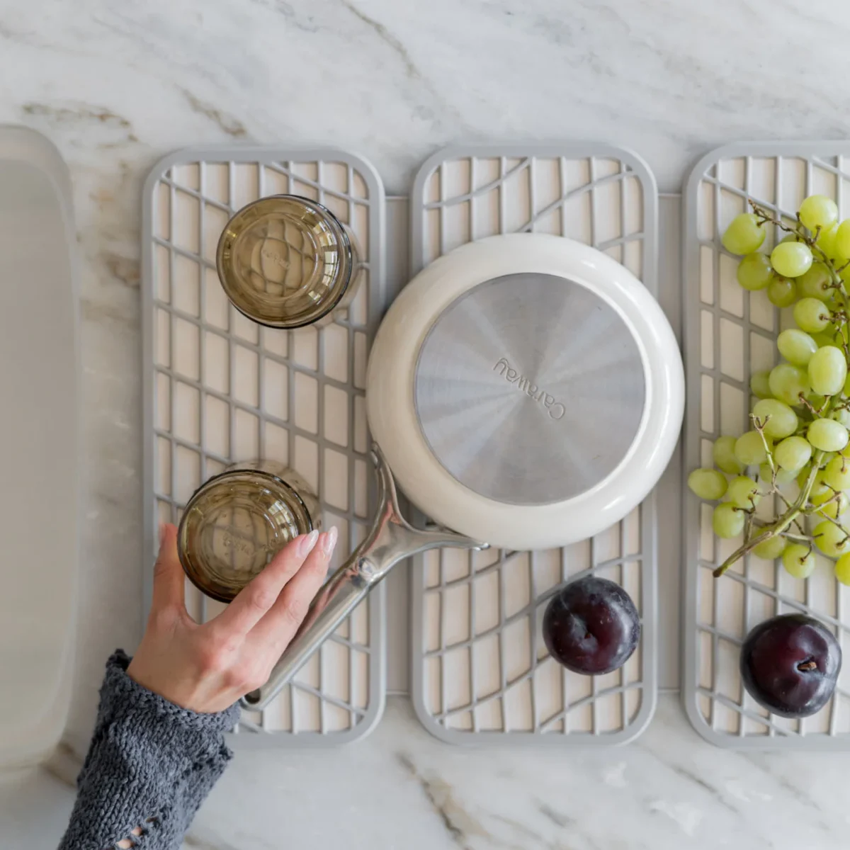 Frau stellt Gläser auf eine Kieselgur Abtropfplatte auf heller Küchenarbeitsplatte neben Herd