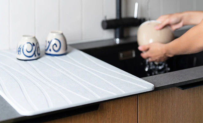 Weiße Kieselgur Abtropfplatte neben Küchenspüle mit nassem Geschirr und tropfendem Wasser