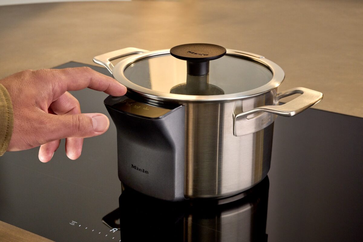 Hand bedient Miele M Sense Sensormodul an Edelstahl-Kochtopf auf Induktionskochfeld