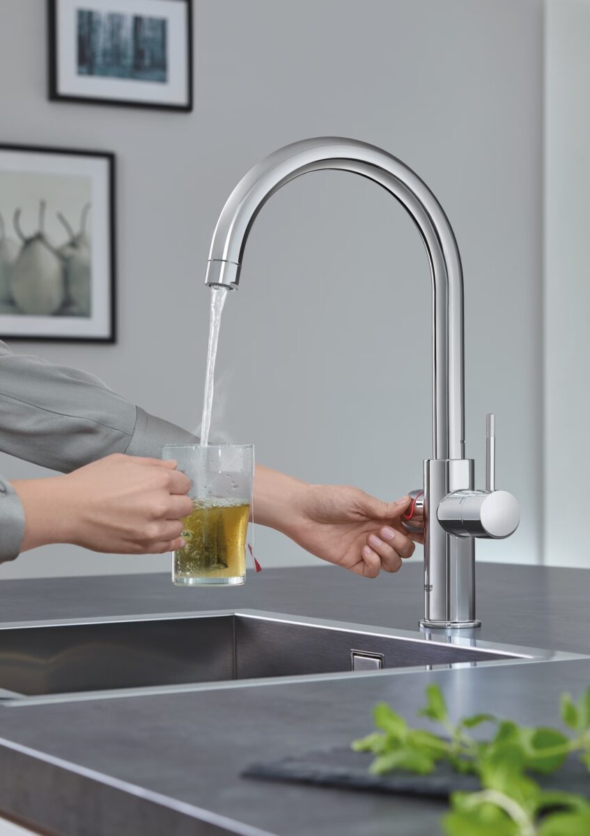 Messingfarbene Armatur mit dampfendem heißem Wasser, das in eine Tasse läuft