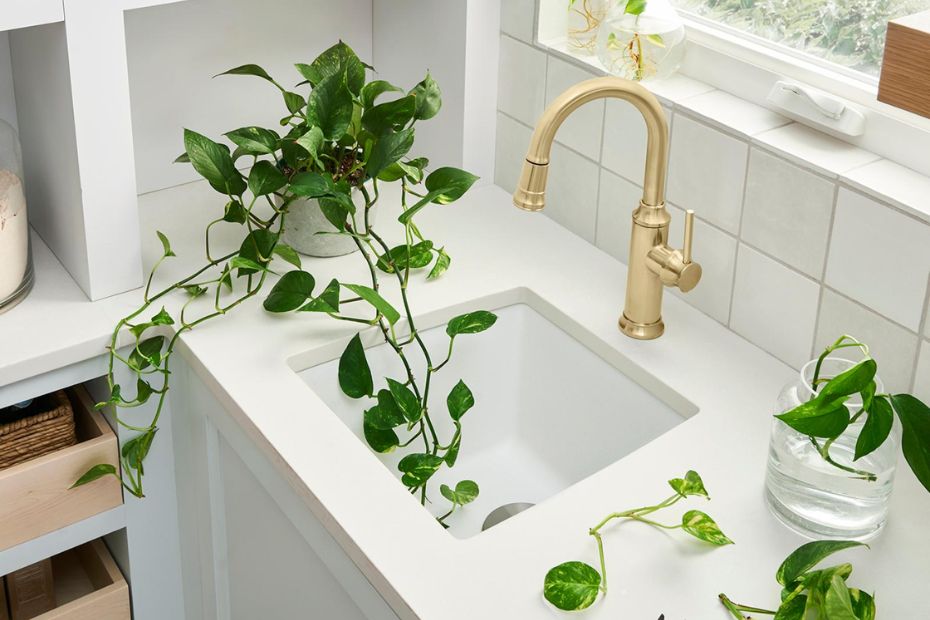 Kleine weiße Zweitspüle mit goldener Armatur und Pflanzen auf heller Arbeitsplatte