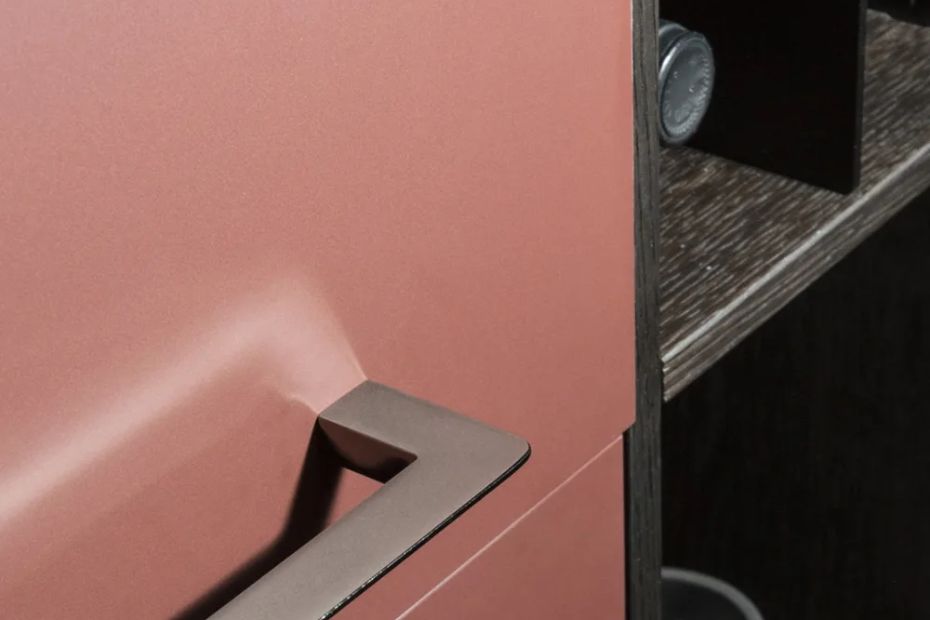 Nahaufnahme einer matten roséfarbenen Küchenfront mit dunklem Griff und seitlicher Kante