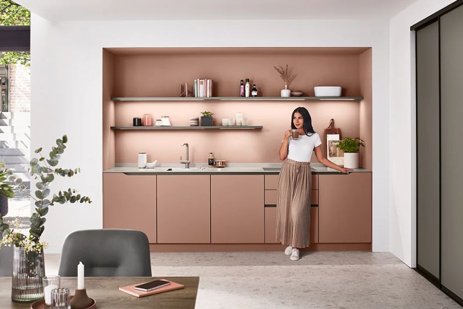 Roséfarbene matte Küchenfronten mit Spüle, offenen Regalen und Person in moderner Küche