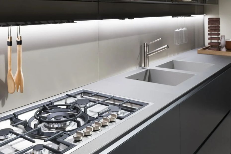 Moderne Küche mit dunklen Fronten, Gaskochfeld, Spüle, heller Arbeitsplatte und beleuchteter Nischenrückwand
