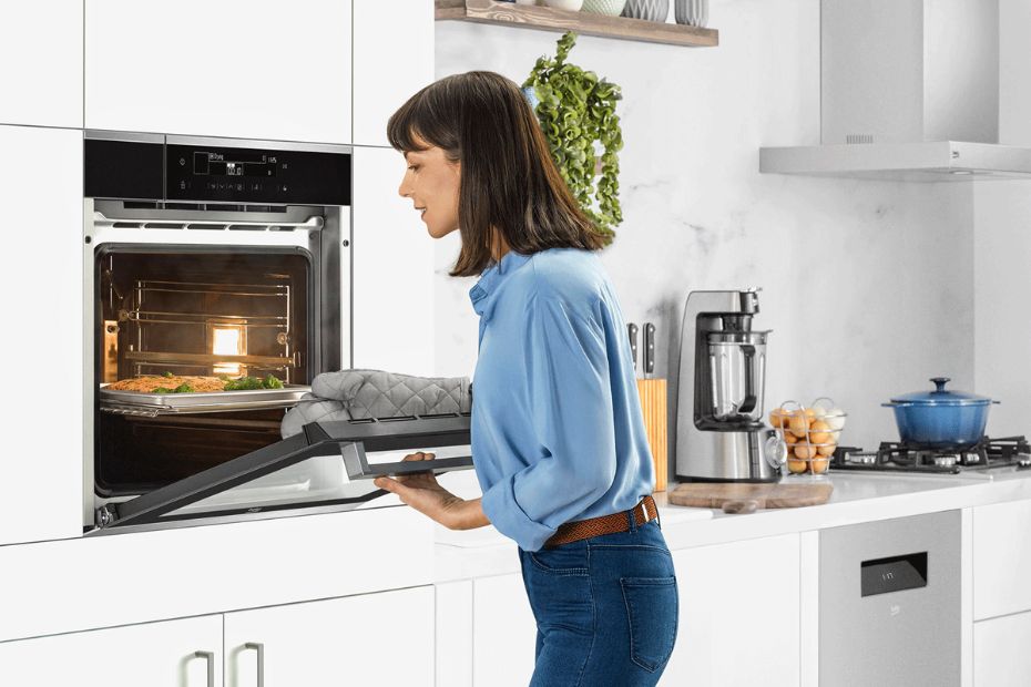 Person öffnet einen Beko Backofen in heller Küche mit Kochfeld und Dunstabzug