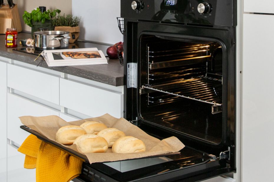 Geöffneter Backofen mit Backblech und Brötchen in weißer Küche