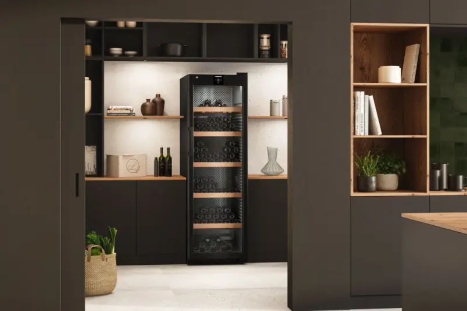 Blick durch einen Durchgang auf einen schwarzen Weinkühlschrank zwischen dunklen Schränken und offenen Regalen