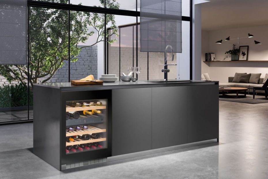 Weinkühlschrank mit Glastür und Holzablagen in einer dunklen Kücheninsel mit Spüle und hoher Armatur