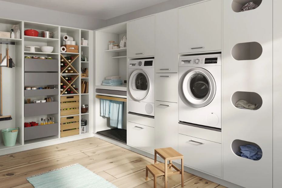 Heller Hauswirtschaftsraum mit erhöhten Geräten, Wäschesortierschrank, Vorratsauszügen und einem Fach für Putzgeräte.