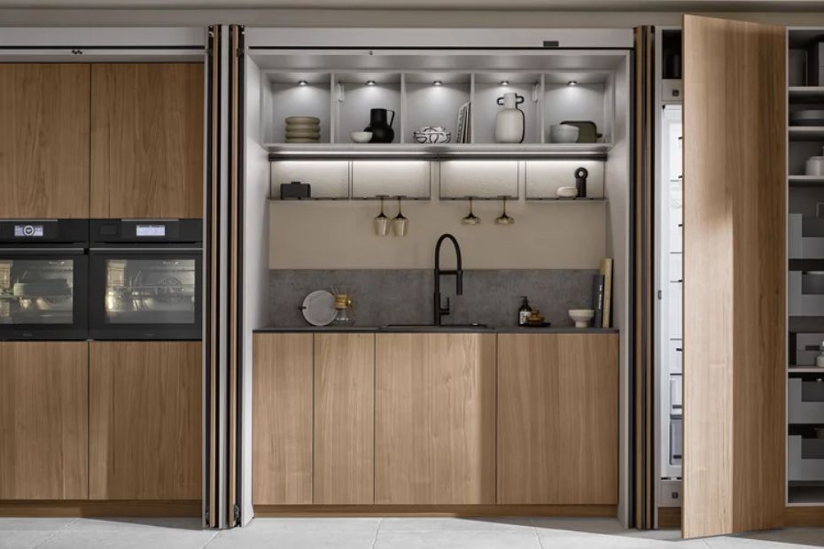 Geöffnete Pocketdoors geben eine Spüle mit schwarzer Armatur, beleuchtete Regale und eine graue Arbeitsfläche frei