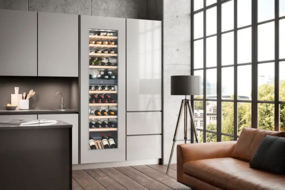 Hoher Weinkühlschrank mit Glastür in einer hellen Hochschrankzeile neben großen Fenstern und einem Sofa